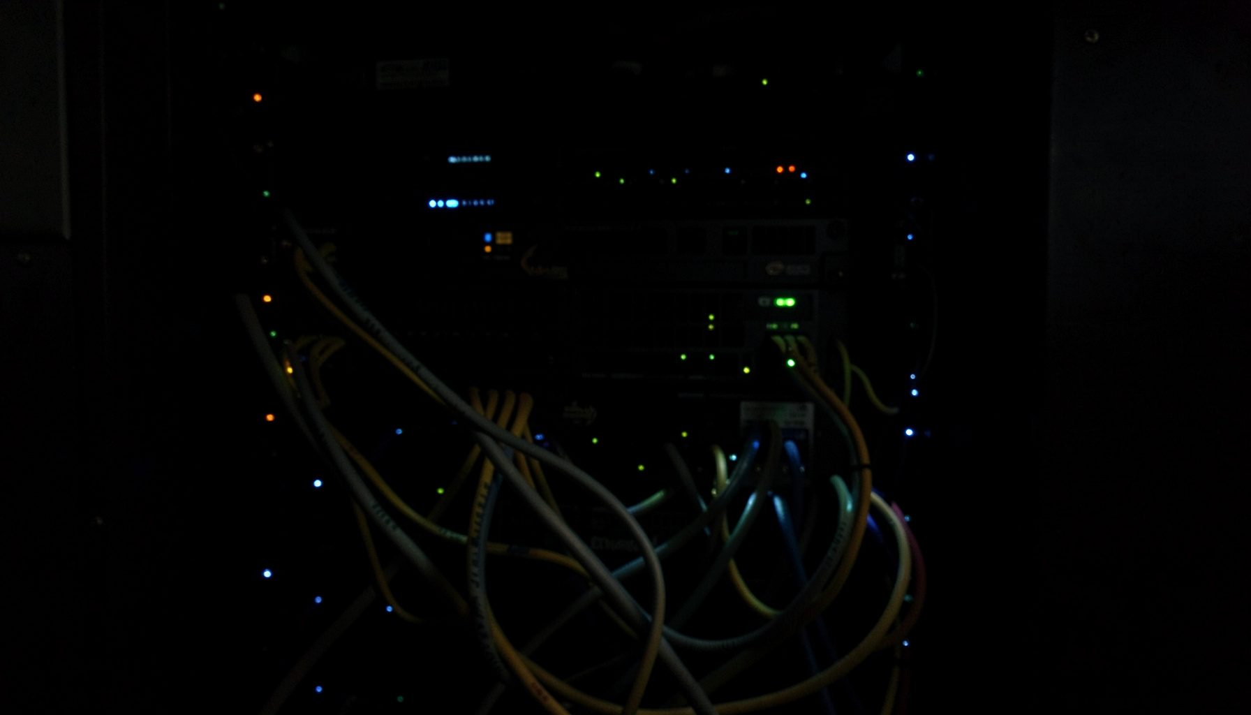 Photographie sombre d'un rack de serveurs réseau illuminé par de minuscules diodes bleues et vertes dans une salle obscure